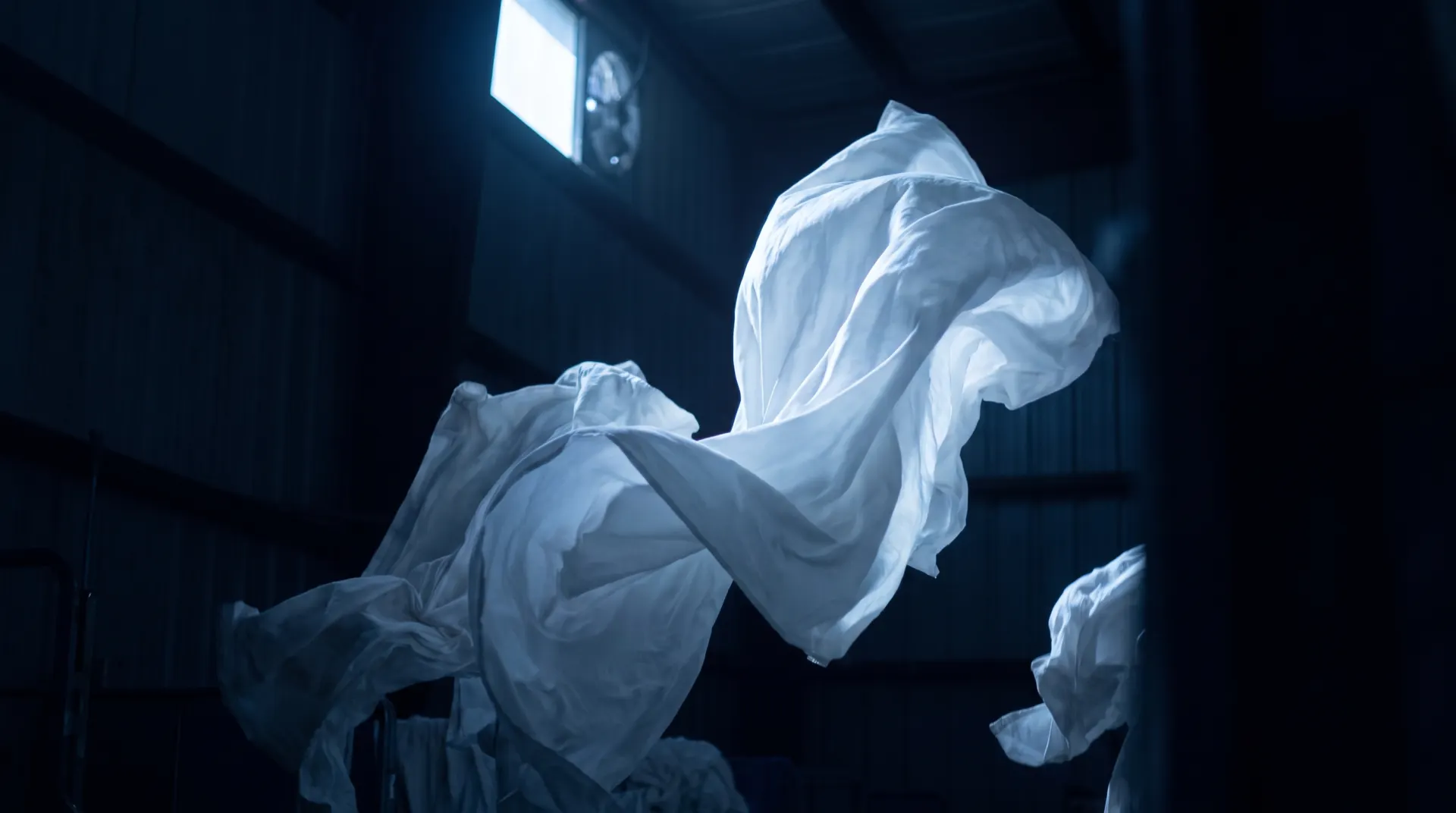 White linen billowing out of deep blue darkness, lit by a single cool light